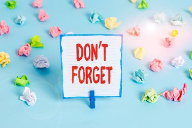 El yazısı metni, unutma. Kavram anlamı, birine önemli bir gerçeği veya detayı hatırlatmak için kullanılır. Renkli buruşmuş kağıtlar boş hatırlatıcı mavi zemin çamaşır mandalı.