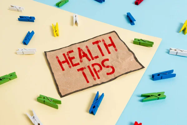 Handwriting text writing Health Tips. Concept meaning beneficial to one s is physical mental or emotional state Colored clothespin paper empty reminder yellow blue floor background office.