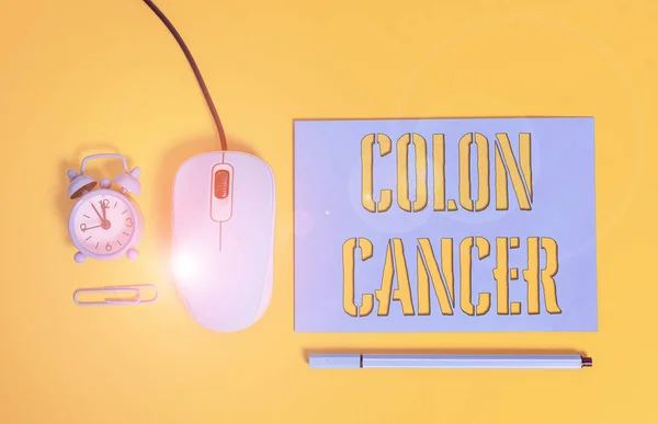 Handwriting text writing Colon Cancer. Concept meaning the development of cancer cells from the colon or rectum Paper sheet alarm clock clip wire mouse gadget pencil colored background.