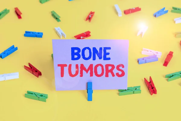 Handwriting text writing Bone Tumors. Concept meaning can be either benign or malignant growths found in the bone Colored clothespin papers empty reminder yellow floor background office. — Stock fotografie