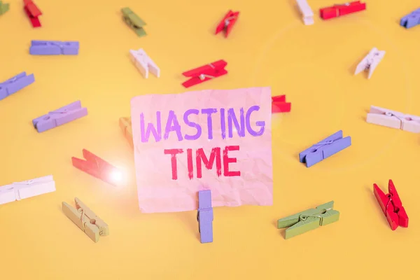 Handwriting text Wasting Time. Concept meaning act of spending time doing something that is unnecessary Colored clothespin papers empty reminder yellow floor background office.