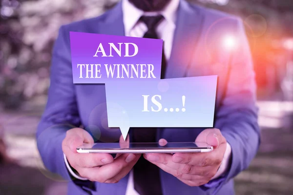 Word writing text And The Winner Is. Businesskonzept zur Bekanntgabe, wer den ersten Platz bei einem Wettbewerb oder einer Prüfung erreicht hat Geschäftsmann in blauer Anzug mit Krawatte hält Laptop in der Hand. — Stockfoto