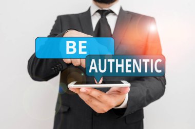 Otantik Ol 'u gösteren kavramsal el yazısı. İş fotoğrafçılığı cesaret isteyen bir şey yap ve kendine karşı dürüst ol. Erkek insan resmi iş kıyafeti giy. Akıllı telefonu kullan..