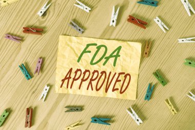 Fda 'nın onaylandığını gösteren bir not yazıyorum. FDA, ürünün ya da formülün güvenli ya da etkili olduğunu kabul etti. Renkli çamaşır iğnesi kağıtları boş ahşap zemin ofisini anımsatıyor..