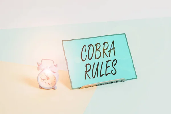 Conceptual hand writing showing Cobra Rules. Business photo showcasing continuing group health insurance coverage after a job loss Alarm clock beside a Paper sheet placed on pastel backdrop.