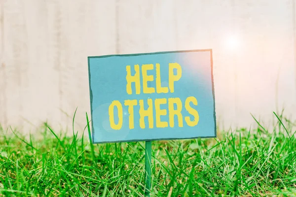 Conceptual hand writing showing Help Others. Business photo showcasing the action of helping someone to do something or assistance Plain paper attached to stick and placed in the grassy land. — Stock Photo, Image