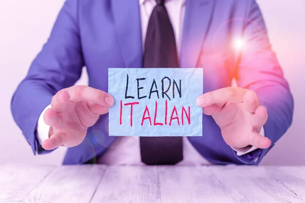 Text sign showing Learn Italian. Conceptual photo gain or acquire knowledge of speaking and writing Italian Man holds empty paper with copy space in front of him Copy Space.