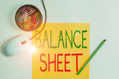 Denge kağıdını gösteren bir not yazıyorum. Şirket varlıklarının borçlarını bildiren iş fotoğraflarının yer aldığı hesap özeti. Not defteri ve arkaplanı pastel olan cihazlar..