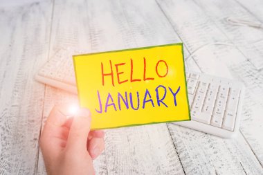 El yazısı. Merhaba Ocak. Kavram, yılın ilk ayına hoş geldin anlamına gelir. Elinde renkli hatırlatıcı kare şeklindeki kağıt beyaz klavye ahşap zemin tutan adama..