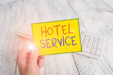 El yazısı otel servisi. Konuklara sıcak konaklama ve renkli hatırlatıcı kare şeklindeki kağıt beyaz klavye ahşap zemin tutan diğer servis elemanlarının konsepti.