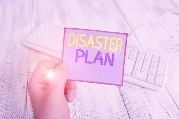 Word writing text Disaster Plan. Business concept for outlines how an organization responds to an unplanned event man holding colorful reminder square shaped paper white keyboard wood floor. — Stock Photo, Image