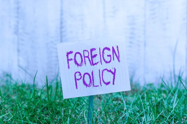 Text sign showing Foreign Policy. Conceptual photo a government strategy in dealing with other nations Plain empty paper attached to a stick and placed in the green grassy land.