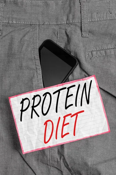 Text sign showing Protein Diet. Conceptual photo low in fat or carbohydrate consumption weight loss plan Smartphone device inside formal work trousers front pocket near note paper.