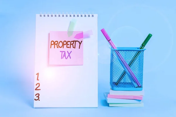 Text sign showing Property Tax. Conceptual photo an ad valorem tax on the value of a property Millage rate Spiral notebook sticky note banners stacked pads pens holder pastel back.