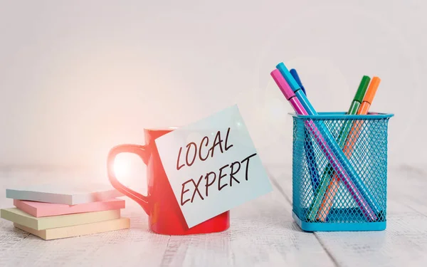 Handwriting text writing Local Expert. Concept meaning offers expertise and assistance in booking events locally Coffee cup blank sticky note pens metal holder stacked pads wooden table.