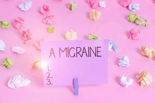 Een handschrift dat A Migraine schrijft. Concept betekent terugkerende kloppende hoofdpijn die een kant van het hoofd beïnvloedt Gekleurde verfrommelde papieren lege herinnering roze vloer achtergrond wasknijper. — Stockfoto