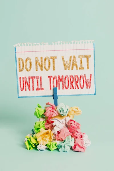 Handwriting text writing Do Not Wait Until Tomorrow. Concept meaning needed to do it right away Urgent Better do now Reminder pile colored crumpled paper clothespin reminder blue background.