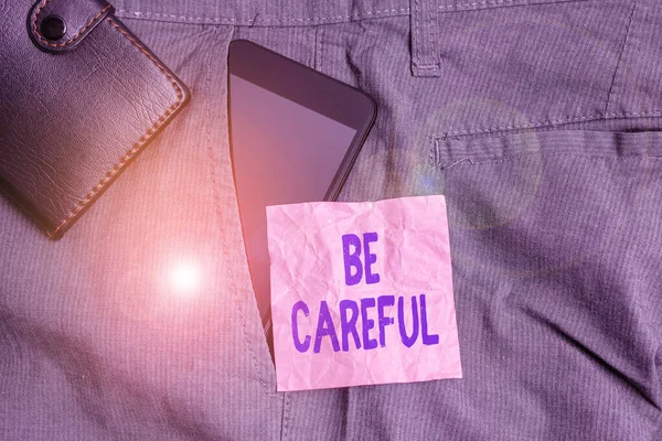 Текстовый знак "Будь осторожен". Концептуальная фотография, чтобы избежать потенциальной опасности несчастный случай или вред смартфон устройство внутри брюк передний карман с бумажником и бумагой для заметок . — стоковое фото