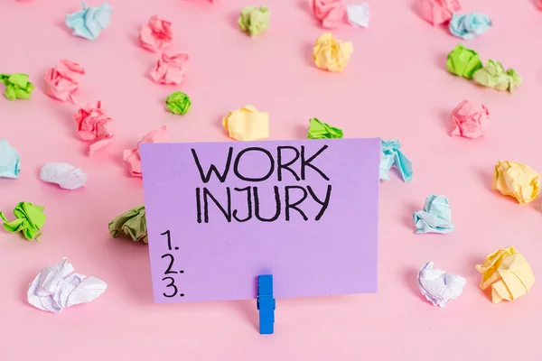 Handwriting text writing Work Injury. Concept meaning illness caused by events or exposures in the work environment Colored crumpled papers empty reminder pink floor background clothespin.