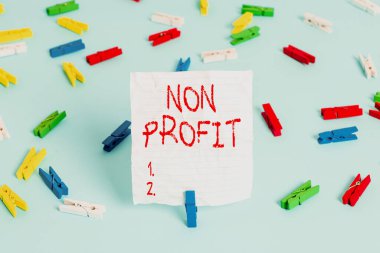 Non Profit 'i gösteren bir not yazıyorum. İş fotoğraflarının sergilenmesi kar amacı gütmüyor ya da yönetilmiyor. Renkli çamaşır iğnesi kağıtları, boş hatırlatma mavi zemin ofisi..