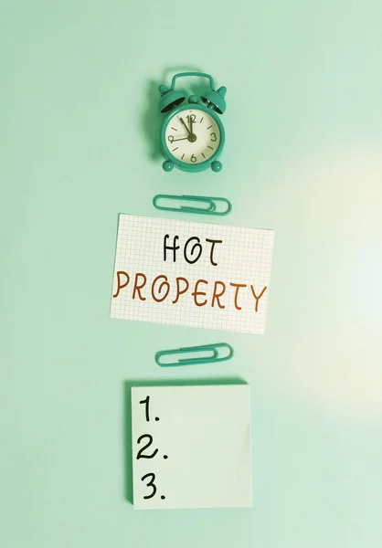 Sinal de texto mostrando Hot Property. Foto conceitual um que muitos mostrando querem comprar e é altamente desejável Relógio despertador quadrado em branco folha de papel clipes bloco de notas fundo colorido . — Fotografia de Stock