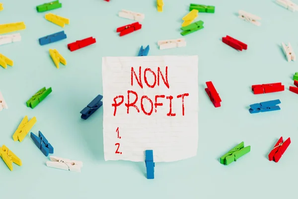 Writing note showing Non Profit. Business photo showcasing not making or conducted primarily to make profit organization Colored clothespin papers empty reminder blue floor officepin.