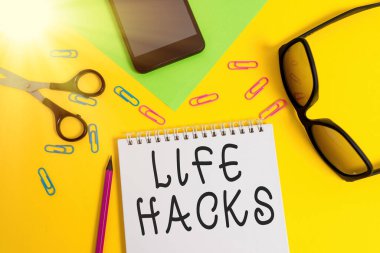Life Hacks 'ı gösteren bir not yazıyorum. Günlük aktiviteleri daha verimli yönetmek için iş fotoğrafı gösterme strateji tekniği kalem akıllı telefon makas gözlük gözlük not renk arkaplan.
