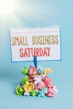 Cumartesi günü Küçük İşletme 'nin el yazısı. Anımsatma sırasında Amerikan alışveriş tatili anlamına gelen kavram. Renkli buruşuk kağıt çamaşır tokası mavi arka planı hatırlatıyor..
