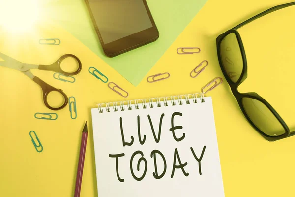 Writing note showing Live Today. Business photo showcasing spend your life doing what you want Live in the present moment Sheet pencil smartphone scissors eyeglasses notepad color background.