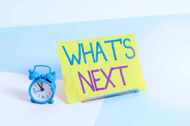 Sırada ne var diye el yazısı. Kavram, gelecekten ya da şu andan itibaren olacaklardan bahsetmek anlamına geliyor. Mini boyunda alarm saati, pastel arka plana yaslanmış kağıt bir çarşaf yanında..