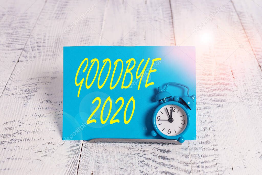 Handwriting text Good Bye 2020. Concept meaning express good wishes when parting or at the end of last year Mini blue alarm clock stand tilted above buffer wire in front of notepaper.
