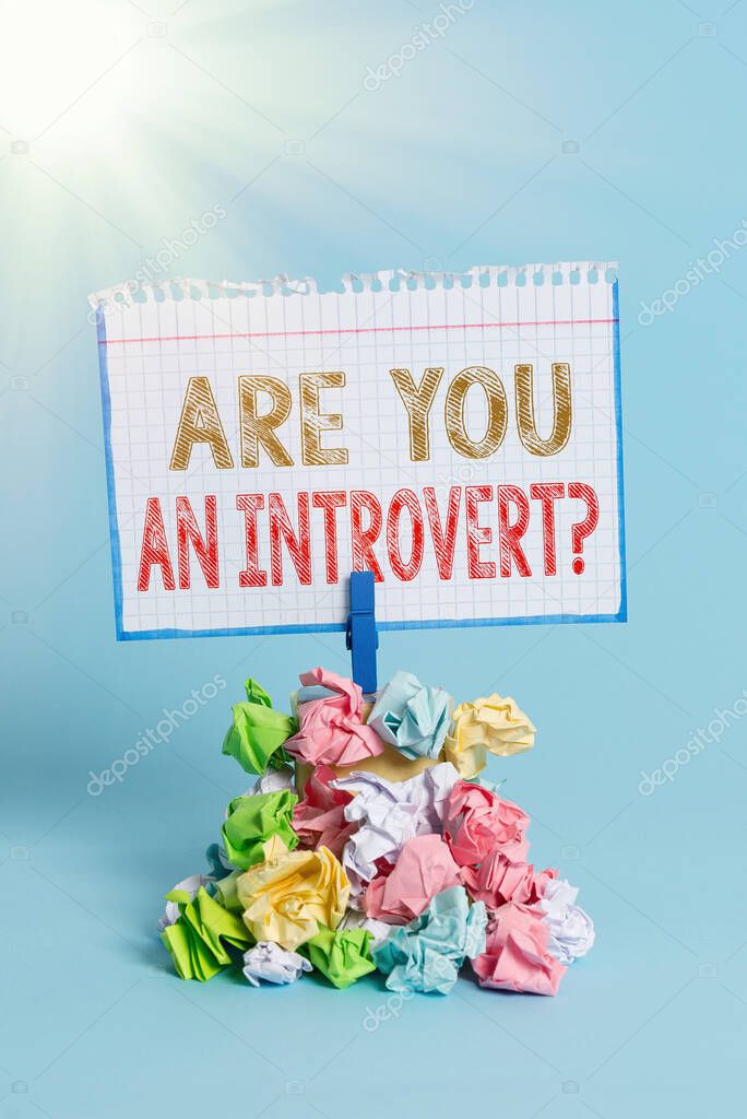 Handwriting text writing Are You An Introvertquestion. Concept meaning demonstrating who tends to turn inward mentally Reminder pile colored crumpled paper clothespin reminder blue background.