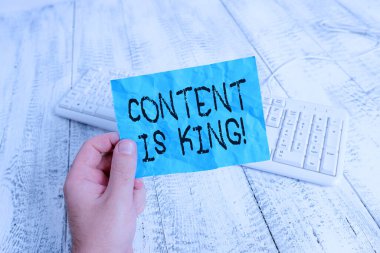 Kelime yazma içeriği kraldır. İş konsepti pazarlama odaklı görünürlük için ödenmemiş arama sonuçları adam renkli hatırlatıcı kare şeklindeki kağıt beyaz klavye ahşap zemin tutuyor.