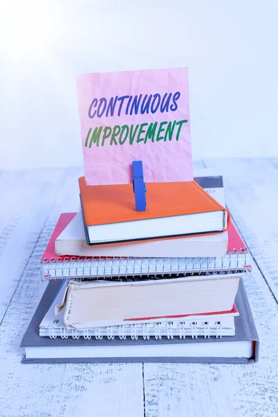 Word writing text Continuous Improvement. Business concept for ongoing effort to improve products or processes pile stacked books notebook pin clothespin colored reminder white wooden.