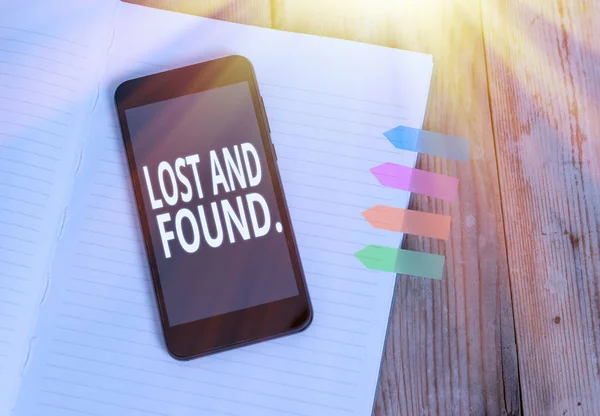 Writing note showing Lost And Found. Business photo showcasing a place where lost items are stored until they reclaimed Striped note book colored arrow banners smartphone wooden background. — Stock Photo, Image