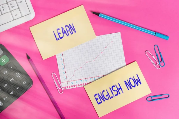 Writing note showing Learn English Now. Business photo showcasing gain or acquire knowledge and skill of english language Writing equipments and computer stuffs placed above colored plain table.