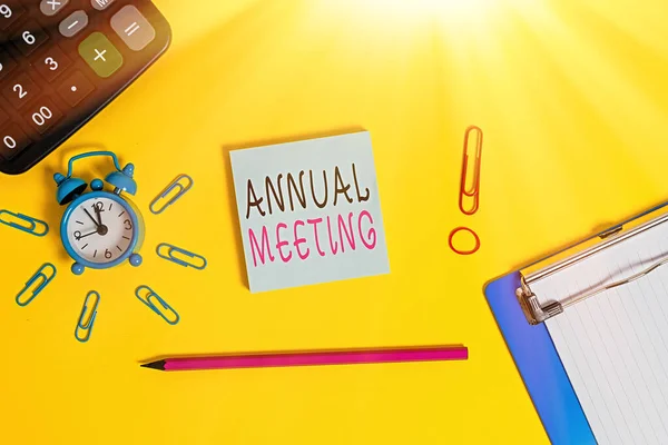 Handwriting text writing Annual Meeting. Concept meaning yearly meeting of the general membership of an organization Alarm clipboard calculator clips band pencil notepad colored background.