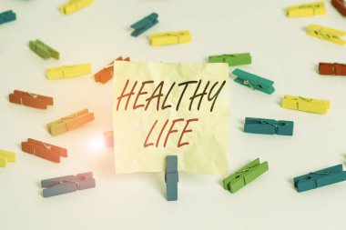 Sağlıklı Yaşam 'ı gösteren bir not yazıyorum. Gösterimlerin korunmasına ve iyileştirilmesine yardımcı olan iş fotoğrafı sergisi sağlık veya durumdur Renkli çamaşır iğnesi kağıtları boş hatırlatıcı beyaz zemin arka plan ofisidir.