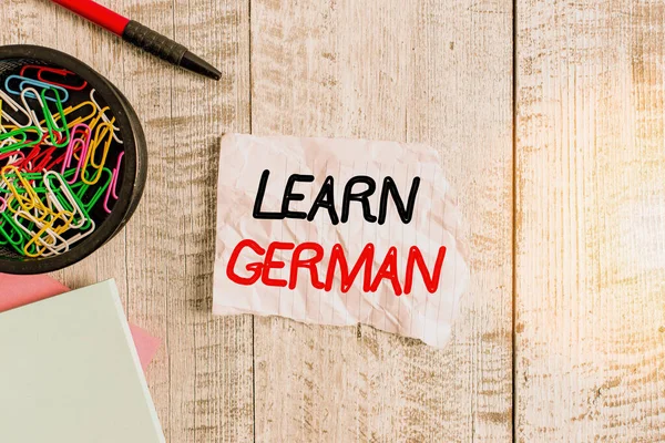 Text sign showing Learn German. Conceptual photo get knowledge or skill in speaking and writing German language Wrinkle paper and notebook plus stationary placed above wooden background.