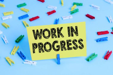 İşlem Devam Ediyor tabelası. Renkli çamaşır iğnesi kağıtlarına eklenen ya da geliştirilen kavramsal fotoğraf tamamlanmamış proje boş hatırlatıcı mavi zemin ofis broşu.