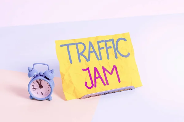 Handwriting text Traffic Jam. Concept meaning a large number of vehicles close together and unable to move Mini size alarm clock beside a Paper sheet placed tilted on pastel backdrop.