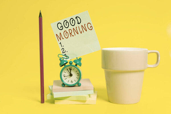 Word writing text Good Morning. Business concept for expressing good wishes on meeting or parting during the morning Alarm clock coffee cup note stacked notepads pencil colored background.
