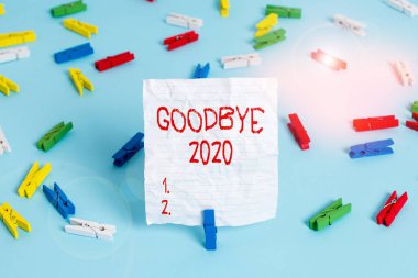 Elveda 2020 'yi gösteren bir not yazıyorum. İş fotoğrafı gösterimi ayrılırken veya geçen yılın sonunda Renkli çamaşır tokası kağıtları boş mavi zemin ofisini hatırlatırken iyi dileklerini iletiyor..