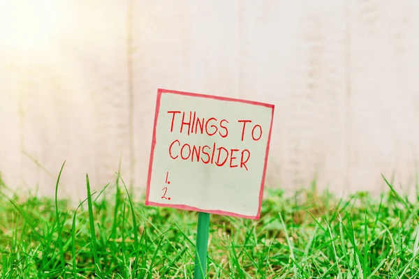 Texto de escritura de palabras Cosas a considerar. Concepto de negocio para pensar en algo cuidadosamente con el fin de tomar una decisión Papel vacío liso pegado a un palo y colocado en la tierra herbácea verde . —  Fotos de Stock