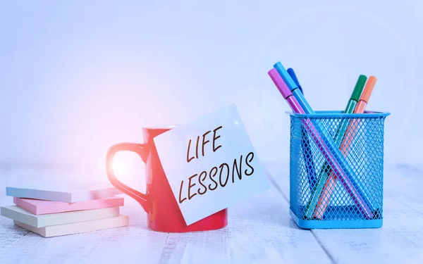 Handwriting text writing Life Lessons. Concept meaning something which useful knowledge or principles can be learned Coffee cup blank sticky note pens metal holder stacked pads wooden table.