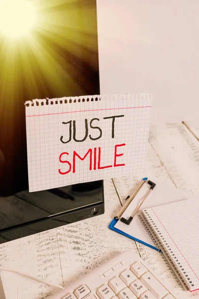 Scrivere una nota che mostra Just Smile. Business photo showcase assumere un'espressione facciale che indica piacere o divertimento Nota carta nastrata sullo schermo del computer nero vicino a tastiera e fermo . — Foto Stock