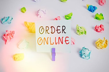 Sipariş Çevrimiçi 'yi gösteren metin işareti. İnternet üzerinden ürün veya hizmet satın almanın kavramsal fotoğraf etkinliği. Renkli buruşmuş kağıtlar boş hatırlatıcı beyaz zemin çamaşır mandalı.