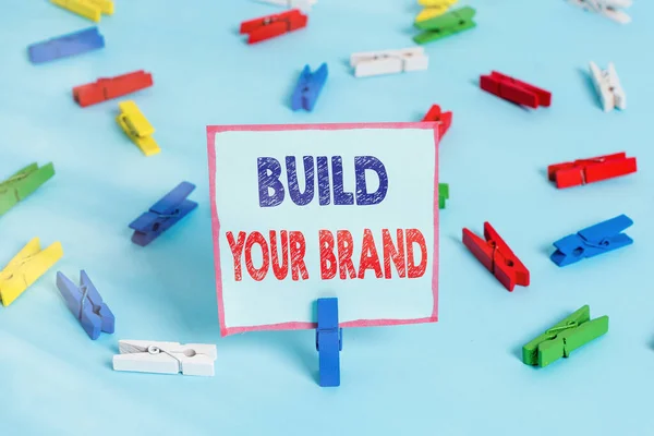 브랜드 구축을 보여 주는 문자 표지판. 광고 캠페인을 사용하여 브랜드의 공정성을 강화하는 컨셉 사진 컬러 클럭 스핀 페이퍼빈 푸른 층 배경 사무실 핀을 상기. — 스톡 사진