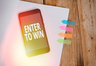 Enter To Win 'i gösteren not yazılıyor. Ticari fotoğraf sergisi ödül ya da ödül için bir şey takas etmek veya Çizgili Kitap renkli ok afişleri akıllı telefon ahşap arka plan.