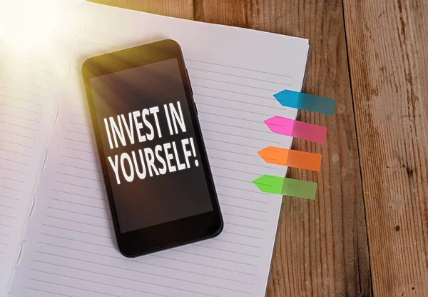 Piszę notatkę z "Inwestuj w siebie". Biznes zdjęcia showcasing nvesting w autokarze lub szkolenia, aby dowiedzieć się nowych rzeczy Pasiasty notatnik kolorowe banery strzałki smartfon drewniane tło. — Zdjęcie stockowe